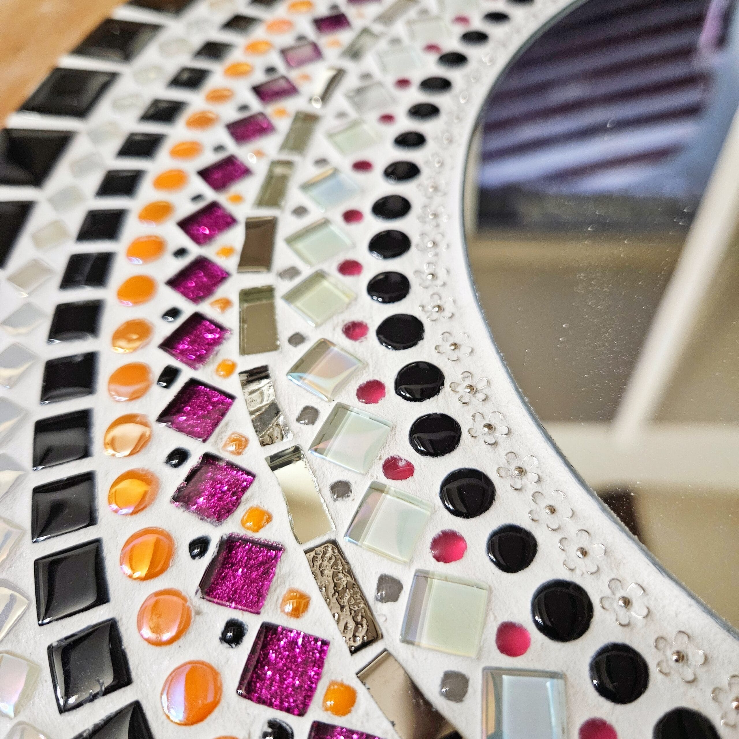 Mosaic mirror with orange, pink and black tiles.